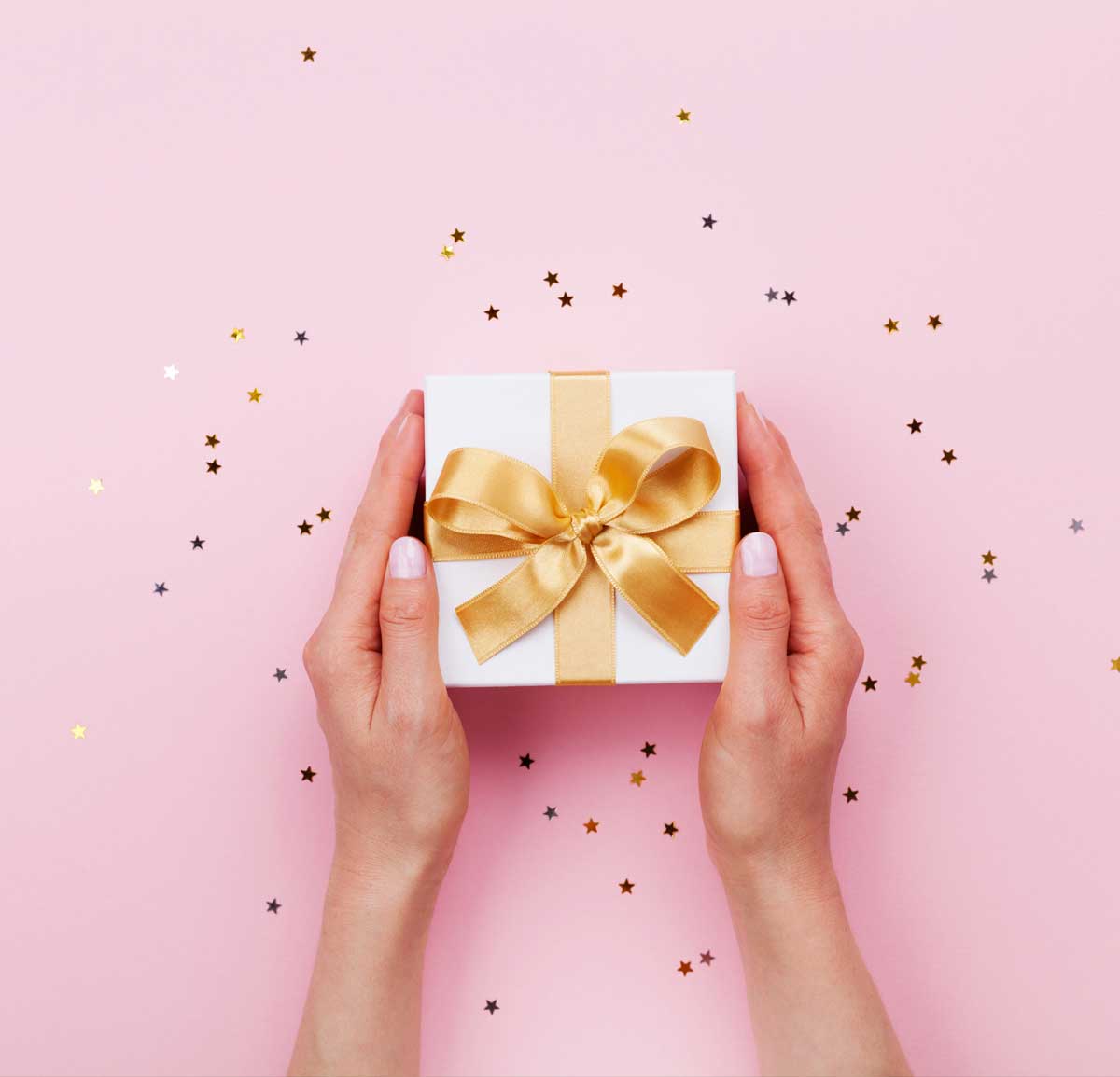 Mains de femme tenant un cadeau sur fond rose et étoiles dorées