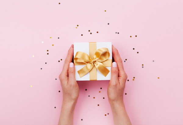 Mains de femme tenant un cadeau sur fond rose et étoiles dorées